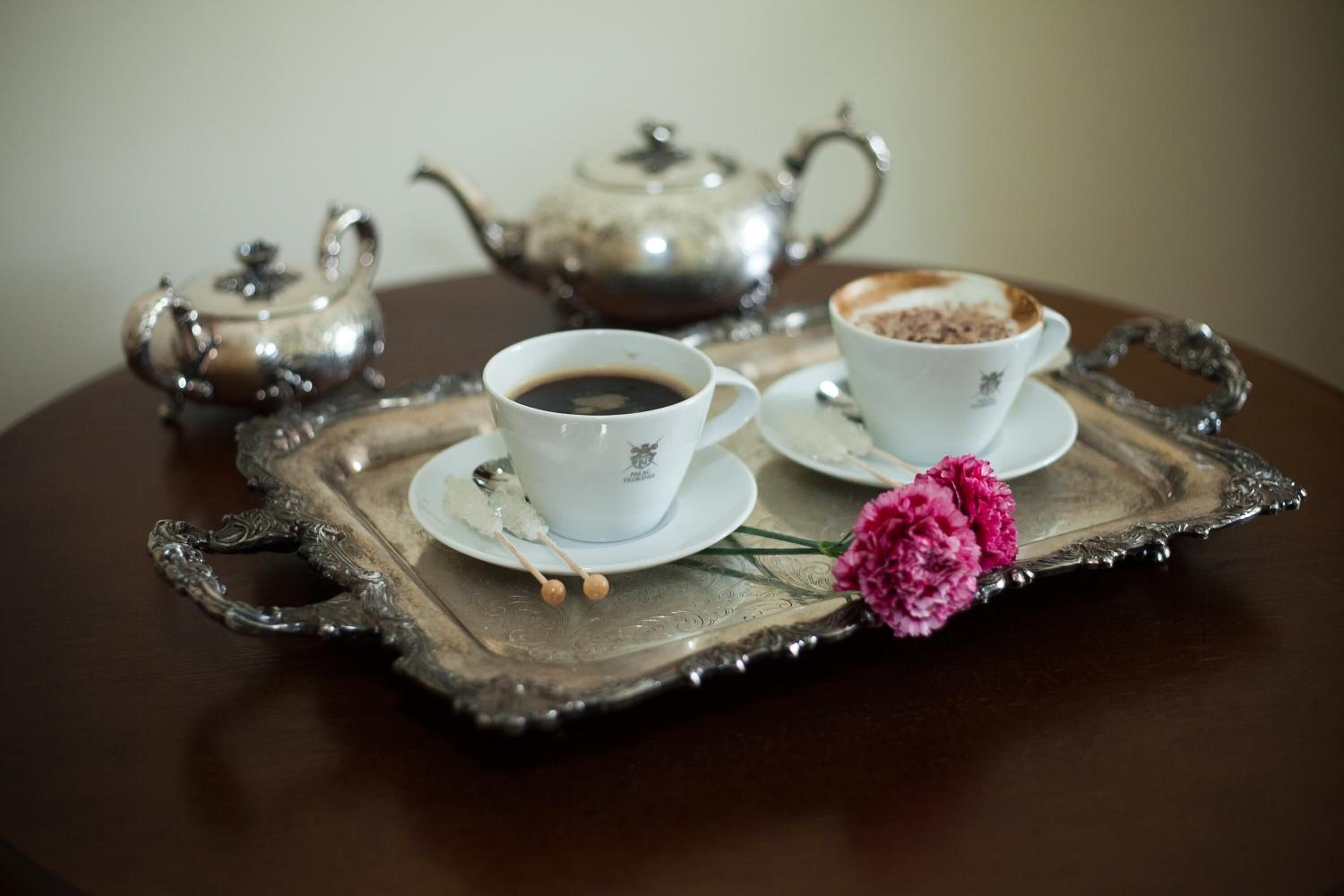 A tray with two cups of coffee, a teapot, and a flower on a wooden table.