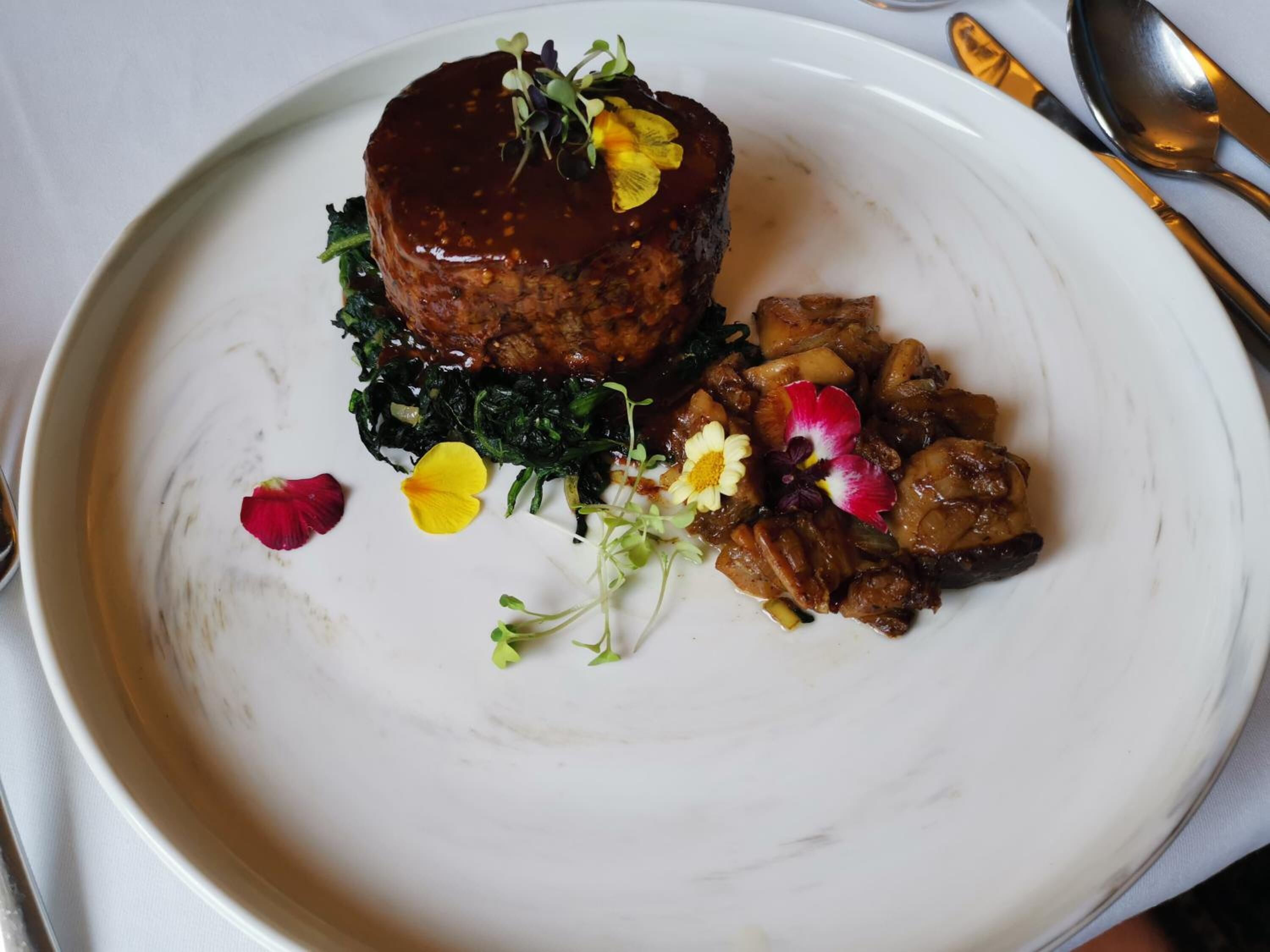 A plate of food with a meat dish, greens, and mushrooms, garnished with flowers.