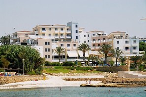 Un hotel frente al mar con varias construcciones, una playa de arena y palmeras.