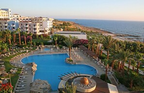 Un resort con una gran piscina, zonas de descanso y vistas al océano.