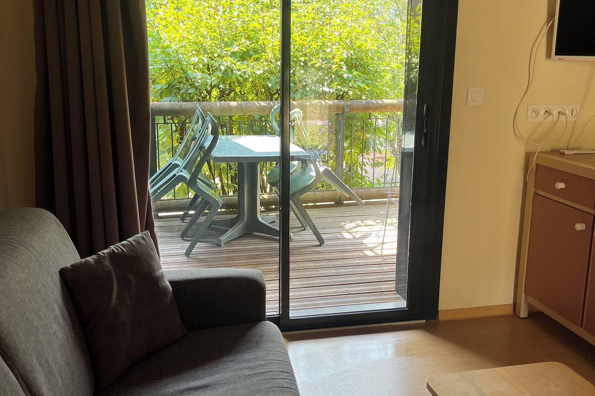 A modern living room with a sofa, a wooden table, and a sliding glass door leading to an outdoor area with a table and chairs.