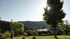 A rural setting with a gravel path leading to a house with a sloped roof, surrounded by greenery and hills in the background. - Domaine Aigoual Cévennes (Meyrueis)