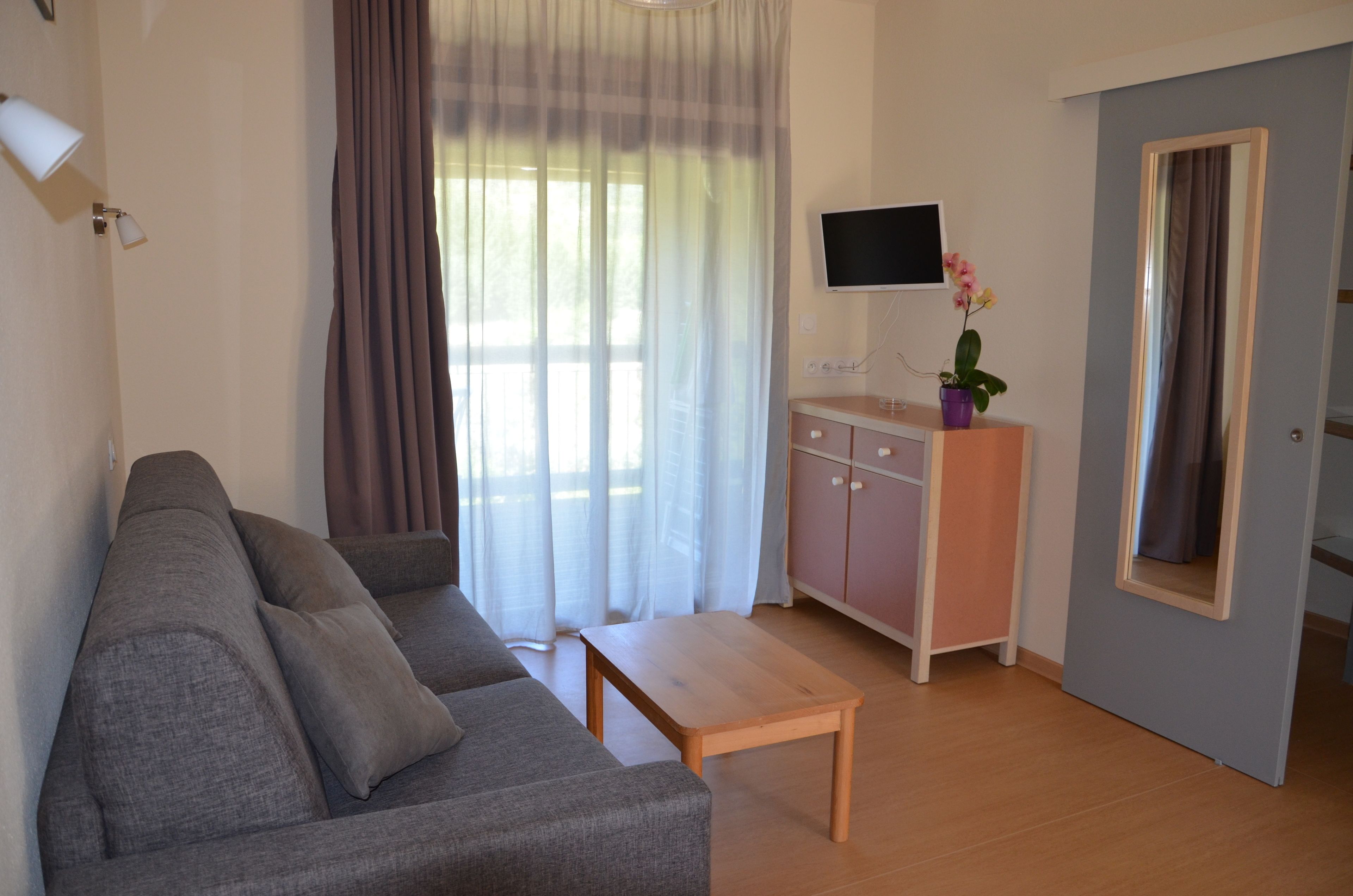 A living room with a sofa, a wooden table, a TV on a stand, a cabinet, and a mirror.