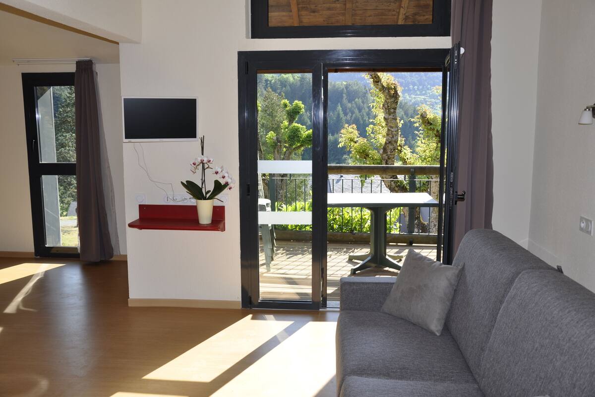 A modern living room with a grey sofa, a red shelf with a potted plant, and a sliding glass door leading to an outdoor patio with a table and chairs.