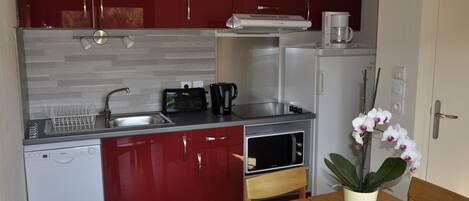 A compact kitchen with red cabinets, a dishwasher, a microwave, and a coffee maker.