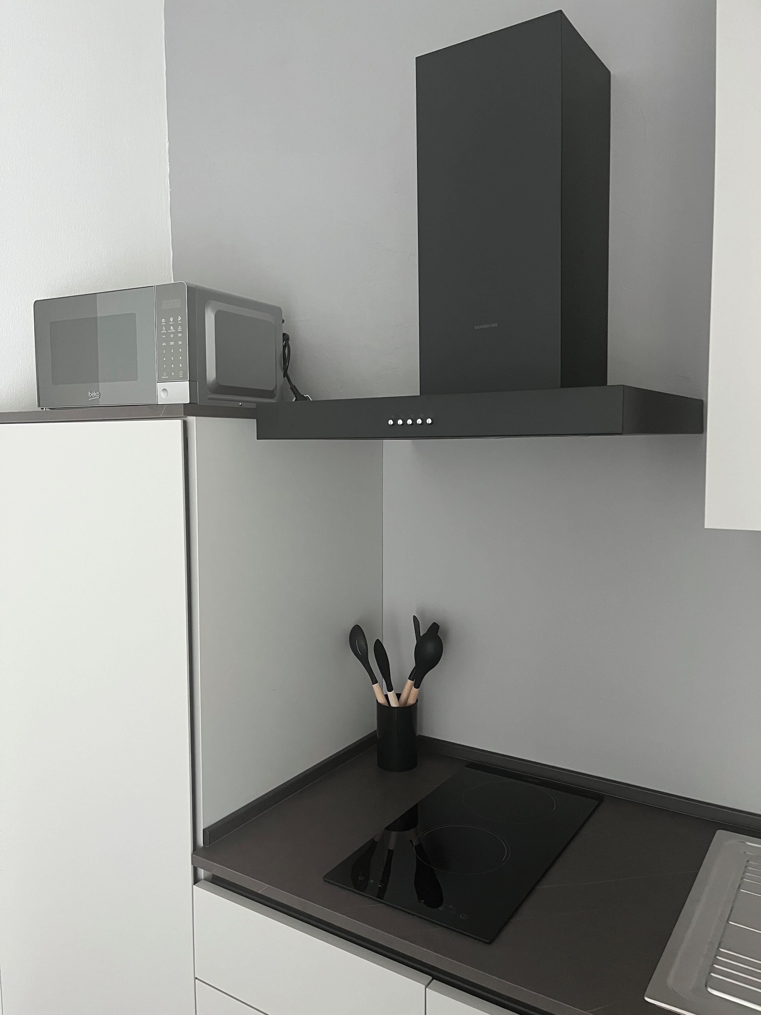 Une cuisine équipée d’un four à micro-ondes, d’une hotte aspirante et d’une plaque de cuisson à induction noire.