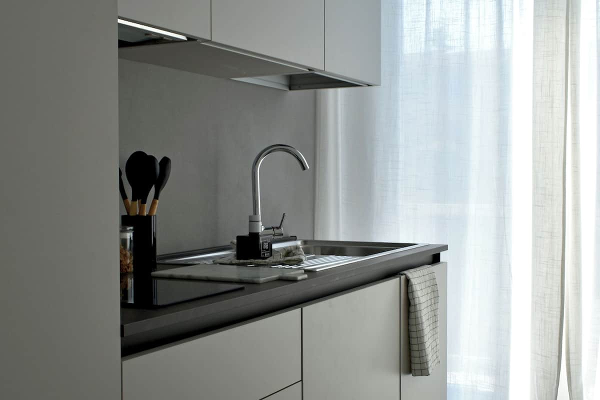 Eine moderne Küche mit Spüle aus Edelstahl, einer schwarzen Arbeitsplatte und einem Fenster mit transparenten Vorhängen.