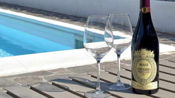 Une bouteille de vin Masi Costasera Amaro Classico et deux verres sur une table près d’une piscine.