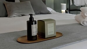 Un lit bien fait, avec des oreillers, un flacon de parfum et une boîte Zara Home posés sur un plateau.