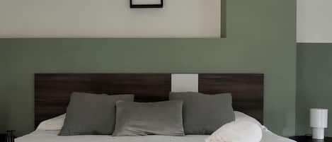 A neatly made bed with pillows, a bedside table with a lamp, and a framed picture on the wall.