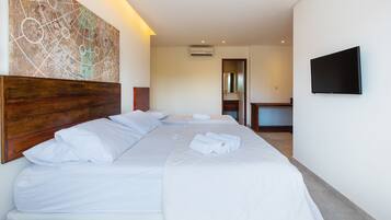 Quarto de hotel com uma cama grande, cabeceira de madeira, televisão de tela plana e ar-condicionado fixado na parede.