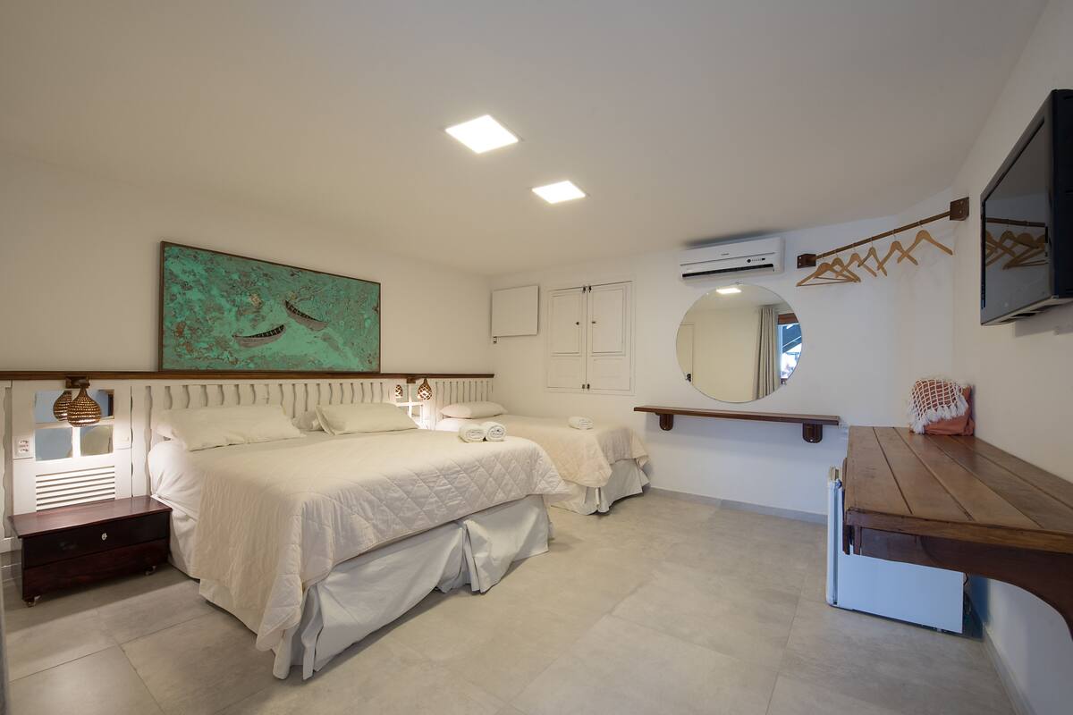 Une chambre avec deux lits, un grand miroir, un banc en bois et un tableau accroché au mur.