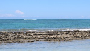 A rocky shoreline with clear blue water and a distant boat. - Pousada Quatro Estações (Ipojuca)