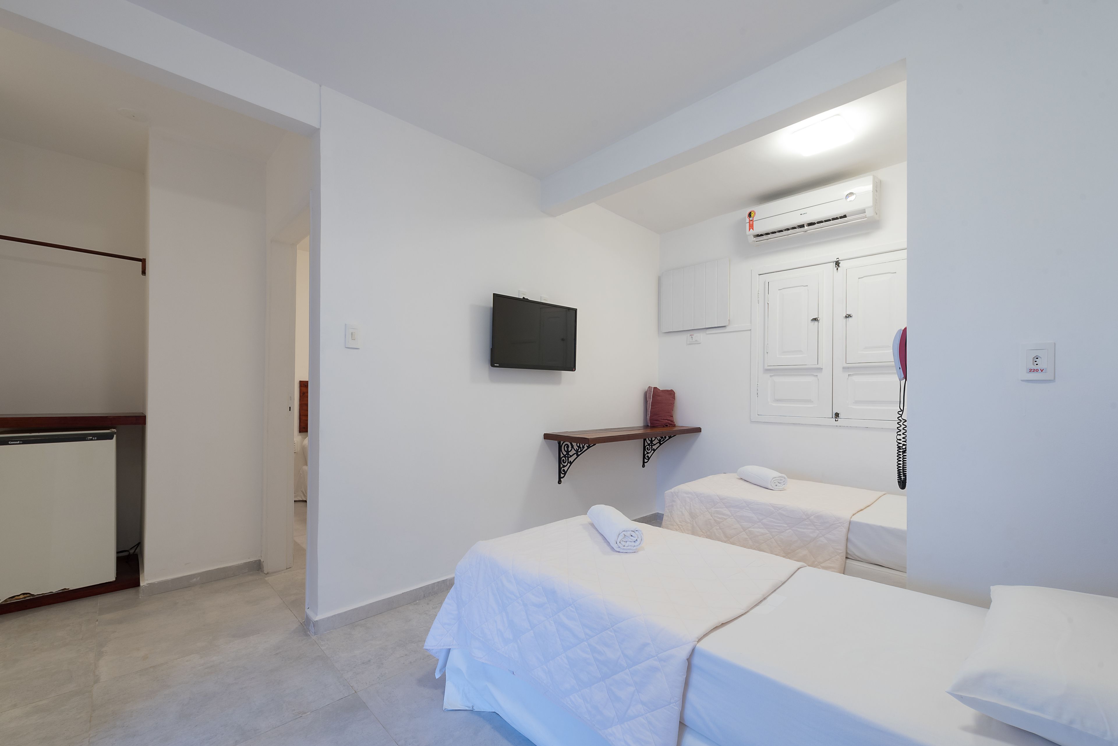 A hotel room with two beds, a TV, an air conditioner, and a wardrobe.