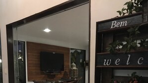 A modern interior with a dining area, a welcome sign, and a television mounted on the wall. - Pousada Quatro Estações (Ipojuca)