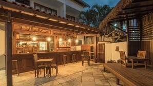 An outdoor bar area with wooden furniture and a thatched-roof structure. - Pousada Quatro Estações (Ipojuca)