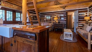 A log cabin interior with a wooden dining table, a sofa, and a wooden cabinet with a sink. - Pioneer Guest Cabins (Crested Butte)