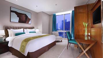 Habitación de hotel con una cama grande, un escritorio, una silla, un televisor y una ventana con cortinas.