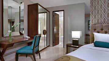 Quarto de hotel com uma cama, uma escrivaninha com cadeira, um espelho, uma mesa de cabeceira com abajur e uma porta para o banheiro.
