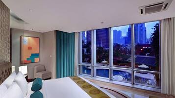 A hotel room with a large bed, a view of the cityscape through large windows, a small seating area, and a painting on the wall.