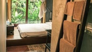 Quarto com cama, escada com toalhas, mosquiteiro e janela com vista para vegetação.