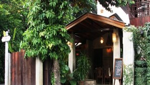 Um edifício rústico com varanda de madeira, uma placa e plantas em vasos.