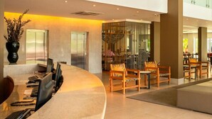 Un hall d’hôtel moderne avec un comptoir d’accueil incurvé, un espace salon et des rampes de protection en verre.