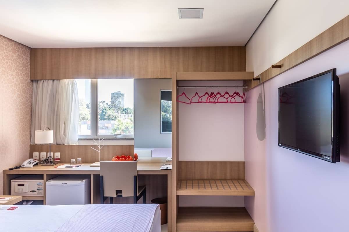 Habitación de hotel con escritorio, silla, cama, televisión y vista a la ciudad.