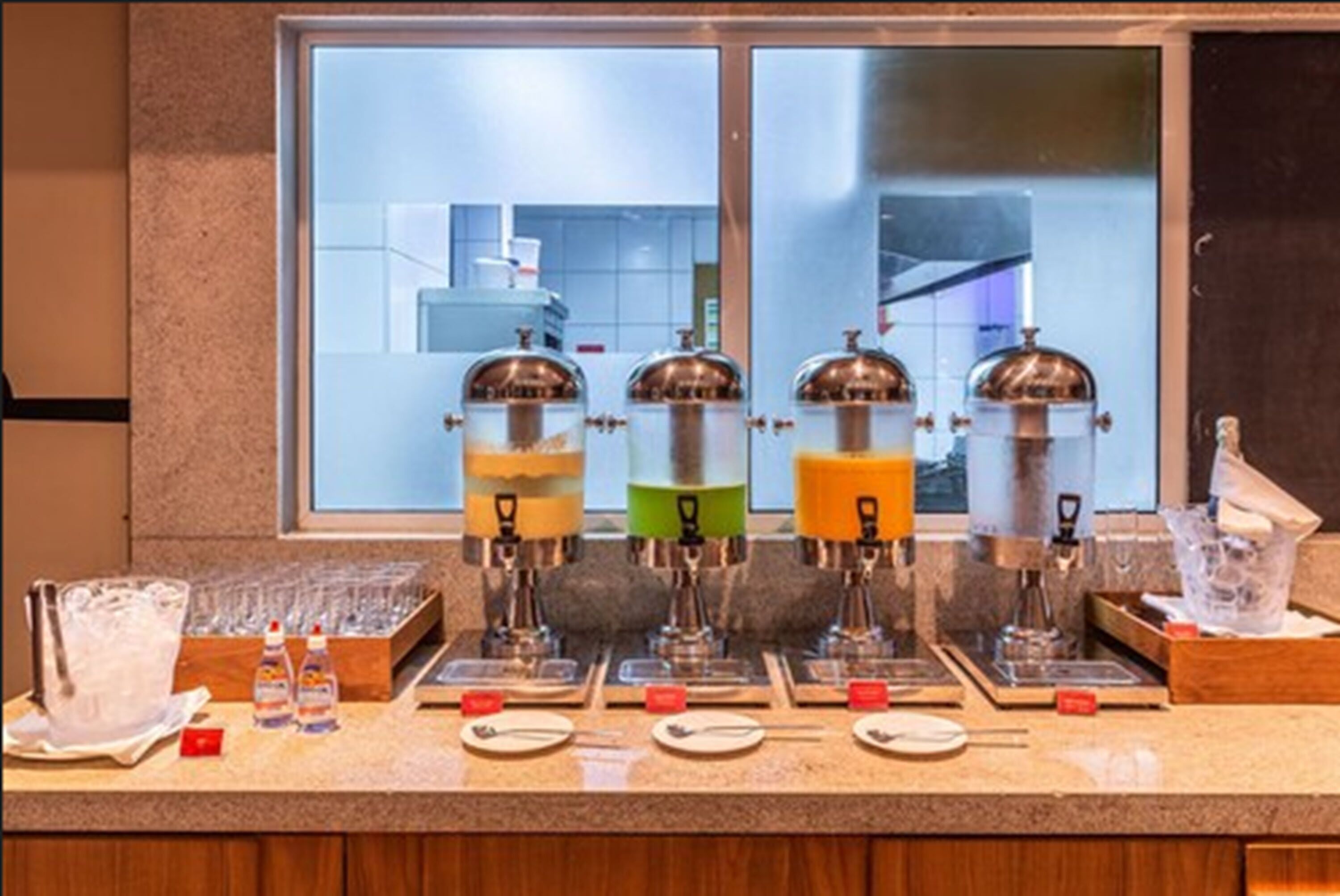 A breakfast bar with multiple beverage dispensers, a variety of utensils, and a window view.