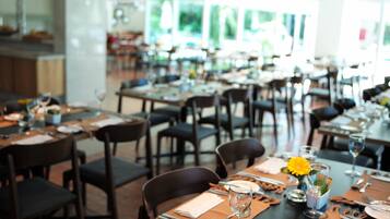 Un restaurante con varias mesas dispuestas para comer, sillas y un jarrón decorativo central con una flor amarilla.