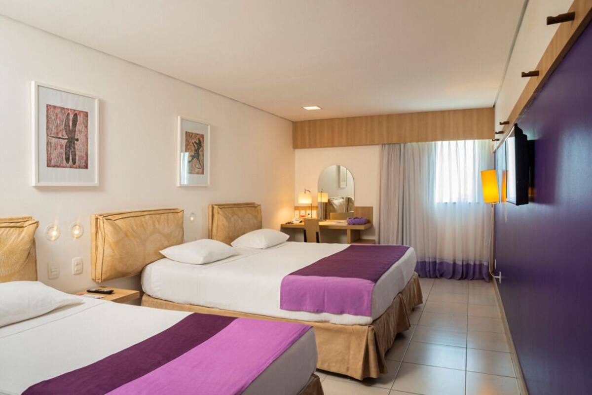 Habitación de hotel con dos camas, un escritorio, una silla, un espejo y un televisor.