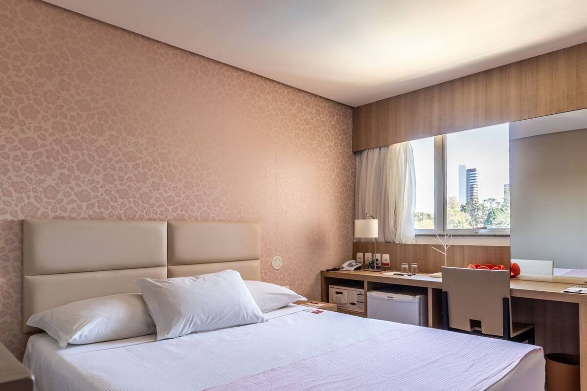 Una habitación de hotel con cama, escritorio, silla y ventana con vista a la ciudad.