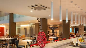 Un moderno vestíbulo de hotel con varias zonas de restauración, una llamativa pieza decorativa roja y una escalera a la vista.