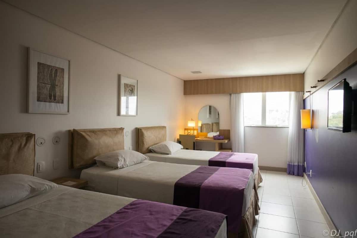 Habitación de hotel con tres camas, un escritorio con silla, un espejo y una ventana con cortinas.
