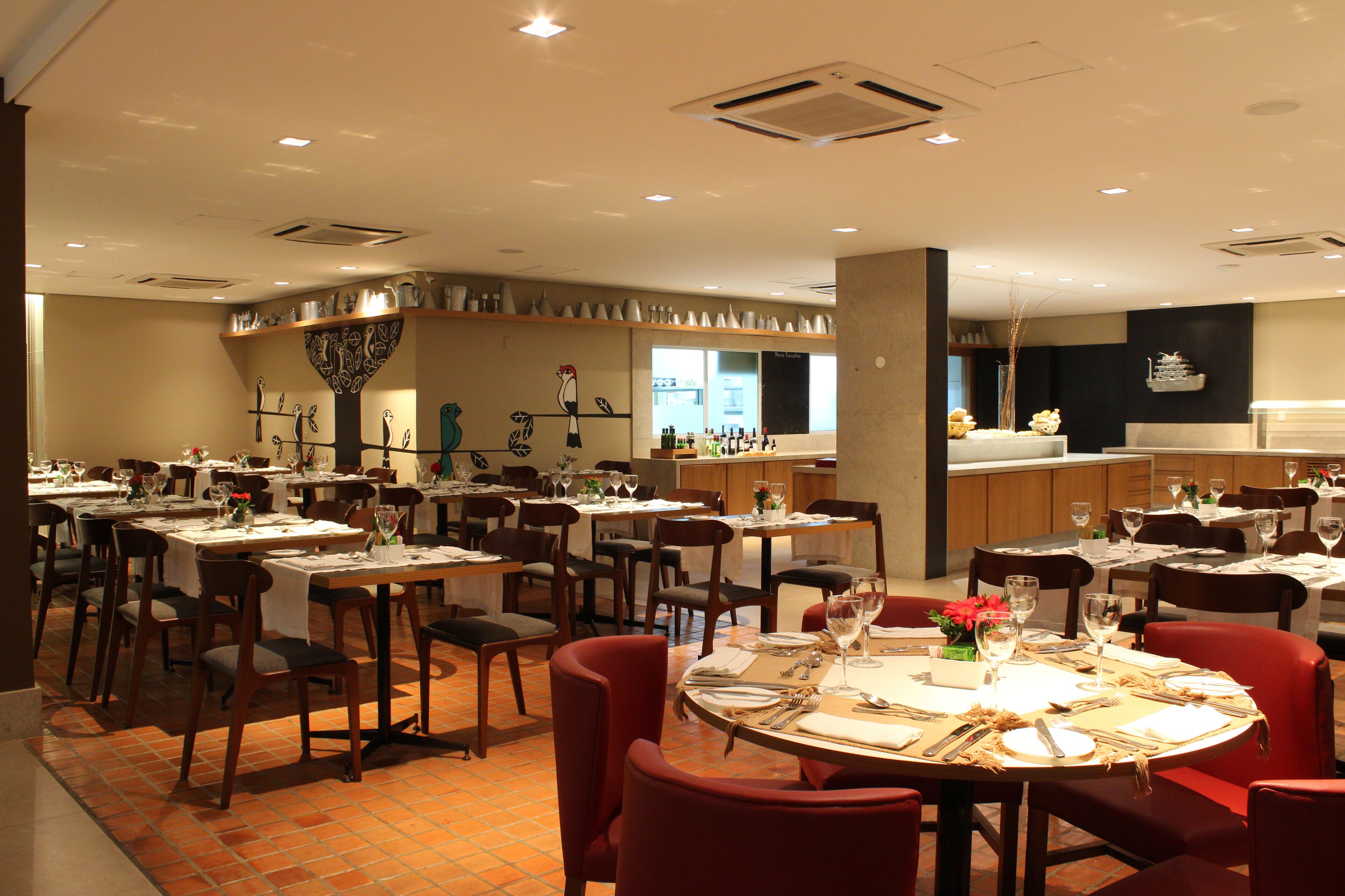 A restaurant with multiple dining tables and chairs, a bar area, and a kitchen in the background.