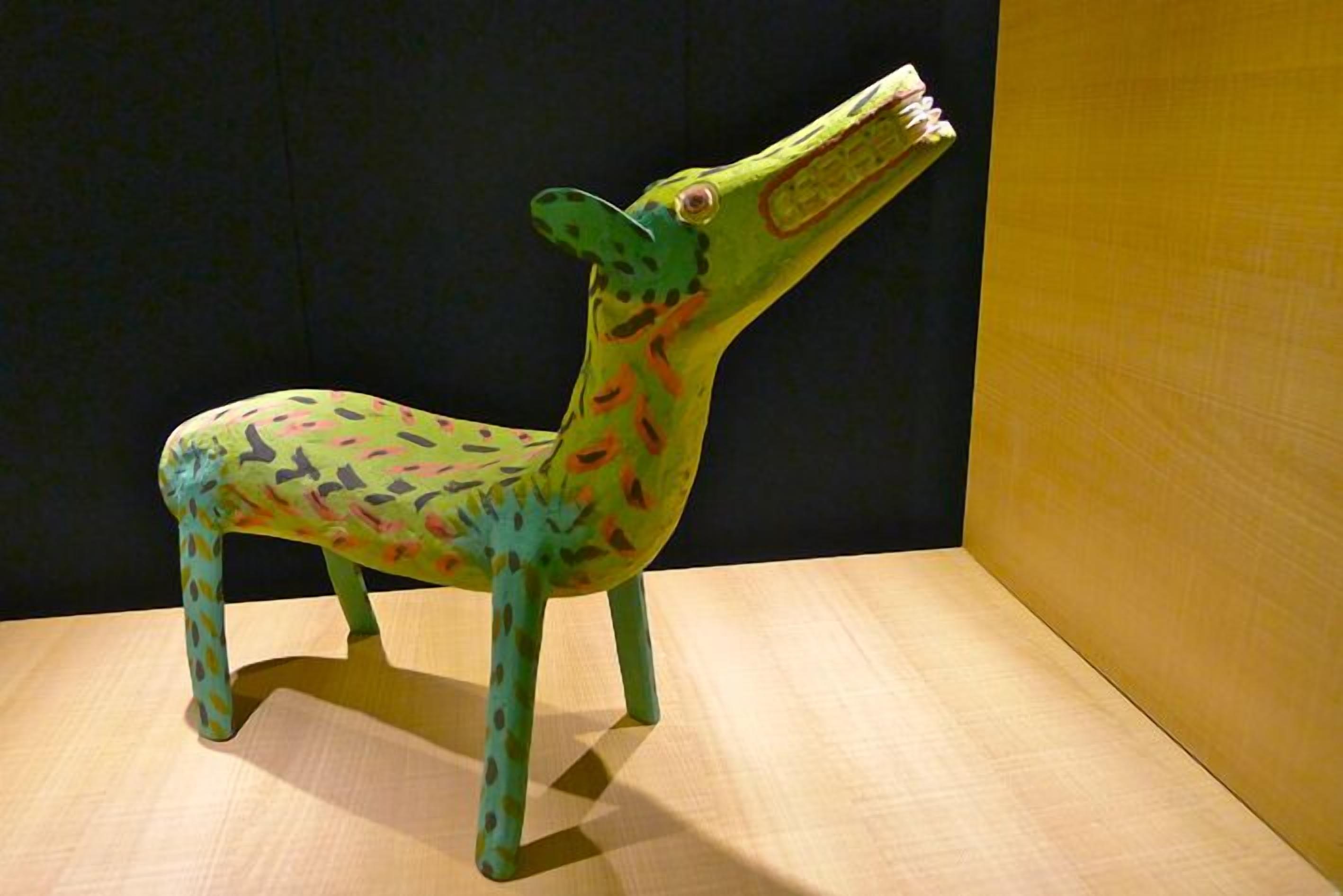 A colorful sculpture of a giraffe on a wooden surface against a dark background.