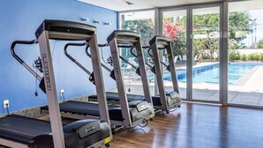 Trois tapis de course sont alignés contre un mur bleu, et une porte vitrée donne accès à un espace piscine.