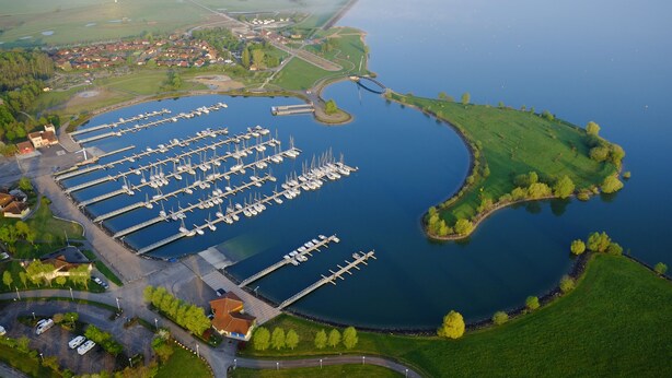 An aerial view of a marina with multiple docks and boats, surrounded by green fields and a small town in the background. - Résidence Marina Holyder (Giffaumont-Champaubert)