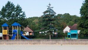 A playground with a blue slide and two small blue-roofed structures, surrounded by trees and houses. - Résidence Marina Holyder (Giffaumont-Champaubert)