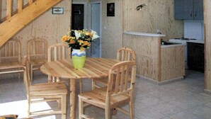 A spacious interior with a high ceiling, wooden staircase, a dining area with chairs, a kitchen area, and a small office space. - Résidence Marina Holyder (Giffaumont-Champaubert)