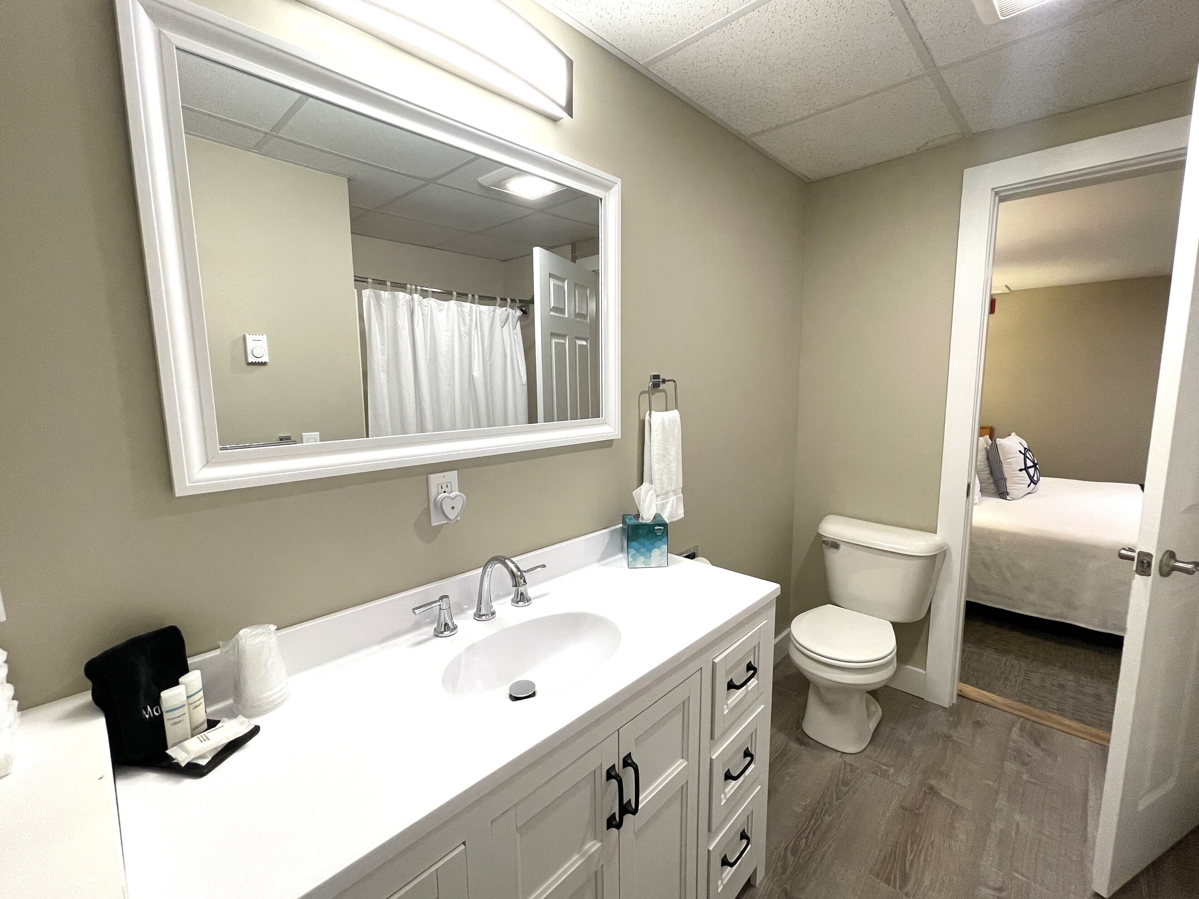 A bathroom with a white sink, mirror, and toilet. There is a towel rack above the sink and a small trash bin beside it.