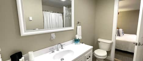 A bathroom with a white sink, mirror, and toilet. There is a towel rack above the sink and a small trash bin beside it.