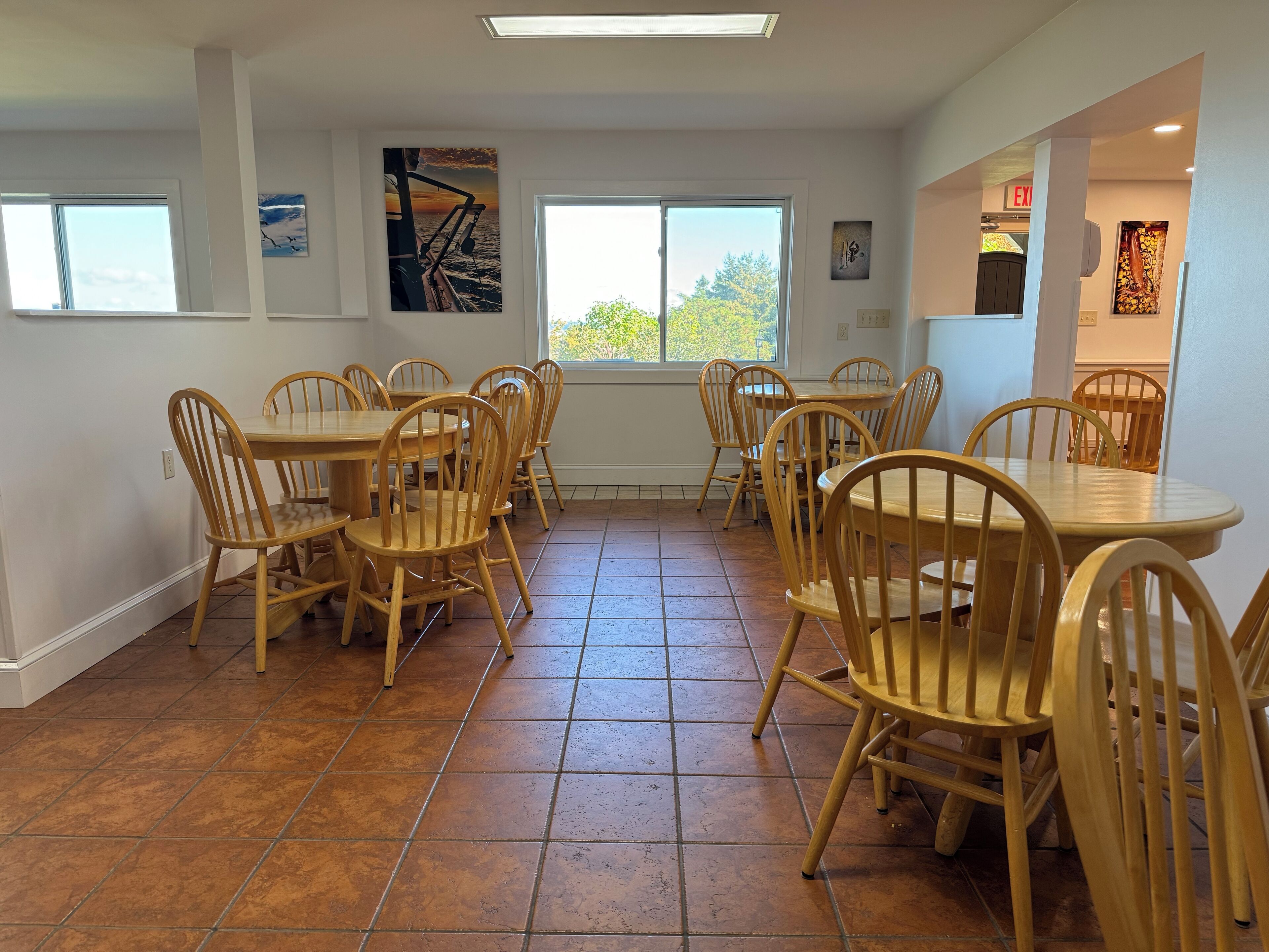 A dining area with wooden tables and chairs, large windows, and artwork on the walls.