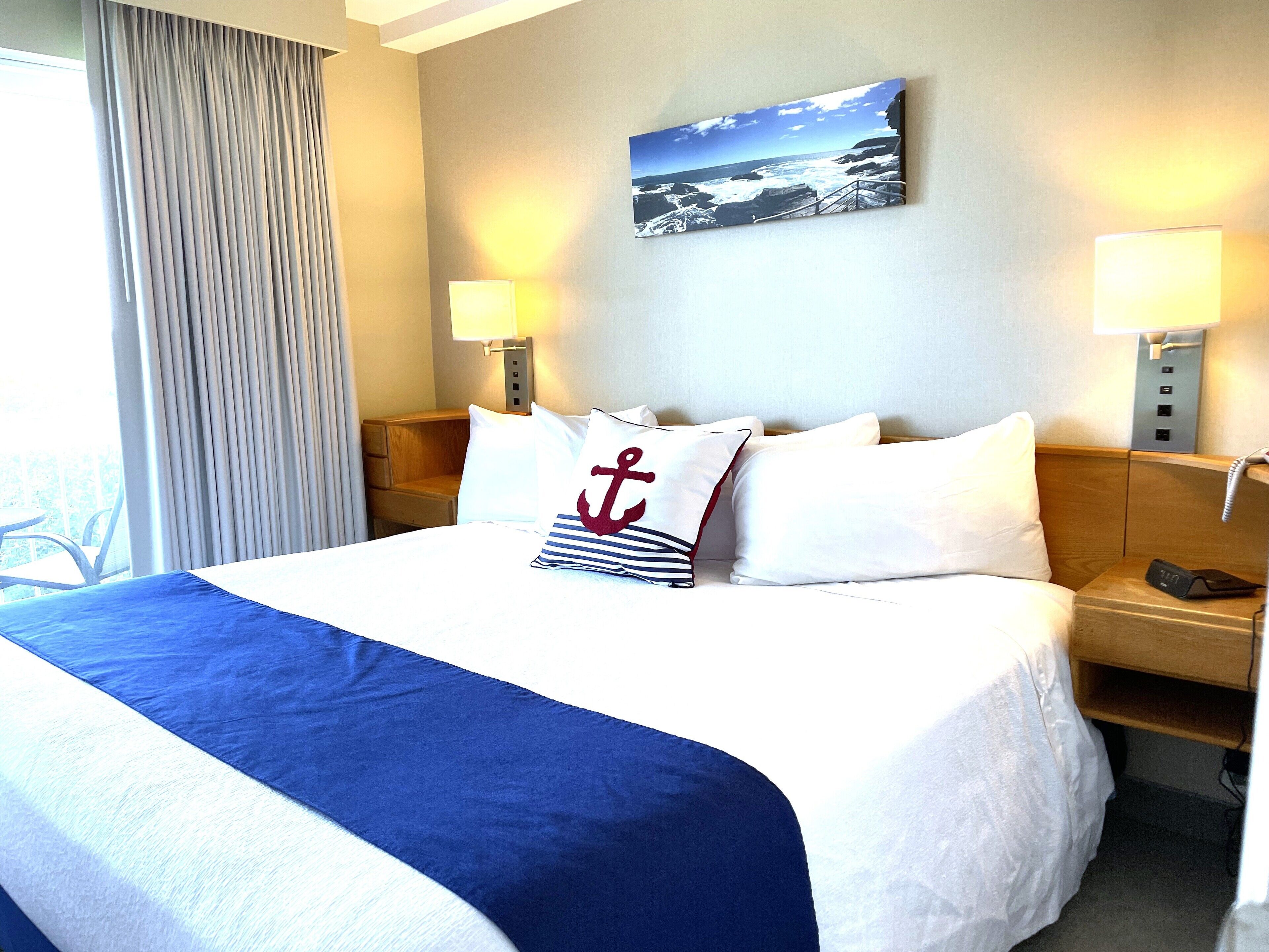 A hotel room with a large bed, a view of the sea, and a wooden nightstand with a phone.