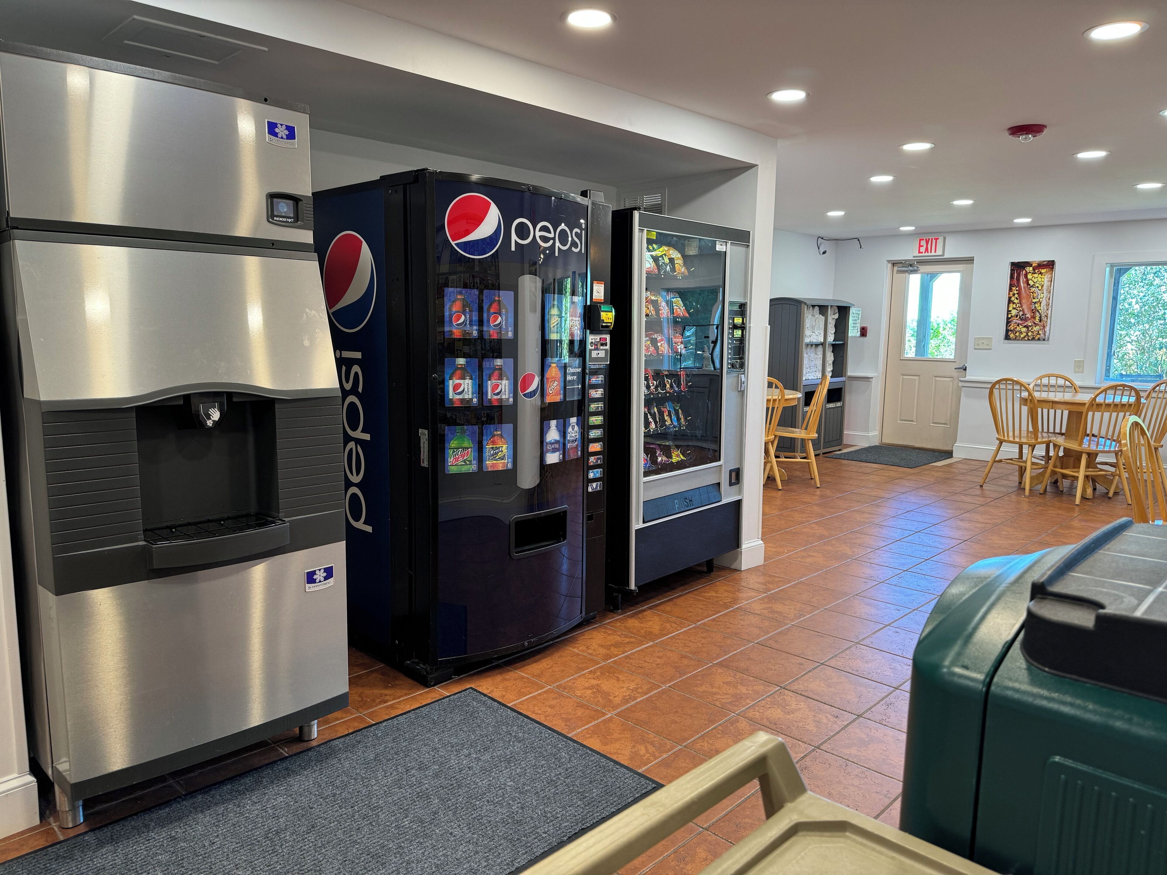 A food court with vending machines, a refrigerator, and a table with chairs.