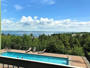 A swimming pool with lounge chairs, surrounded by a fence, overlooking a body of water and distant mountains. - Atlantic Eyrie Lodge (Bar Harbor)