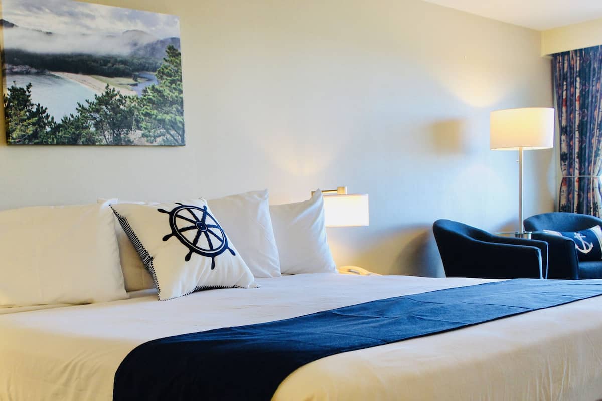 Quarto de hotel com uma cama, uma cadeira, um abajur e um quadro na parede.
