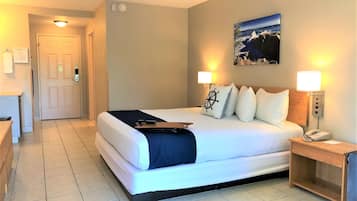 A hotel room with a bed, bedside lamps, a nightstand, a painting on the wall, and a door.
