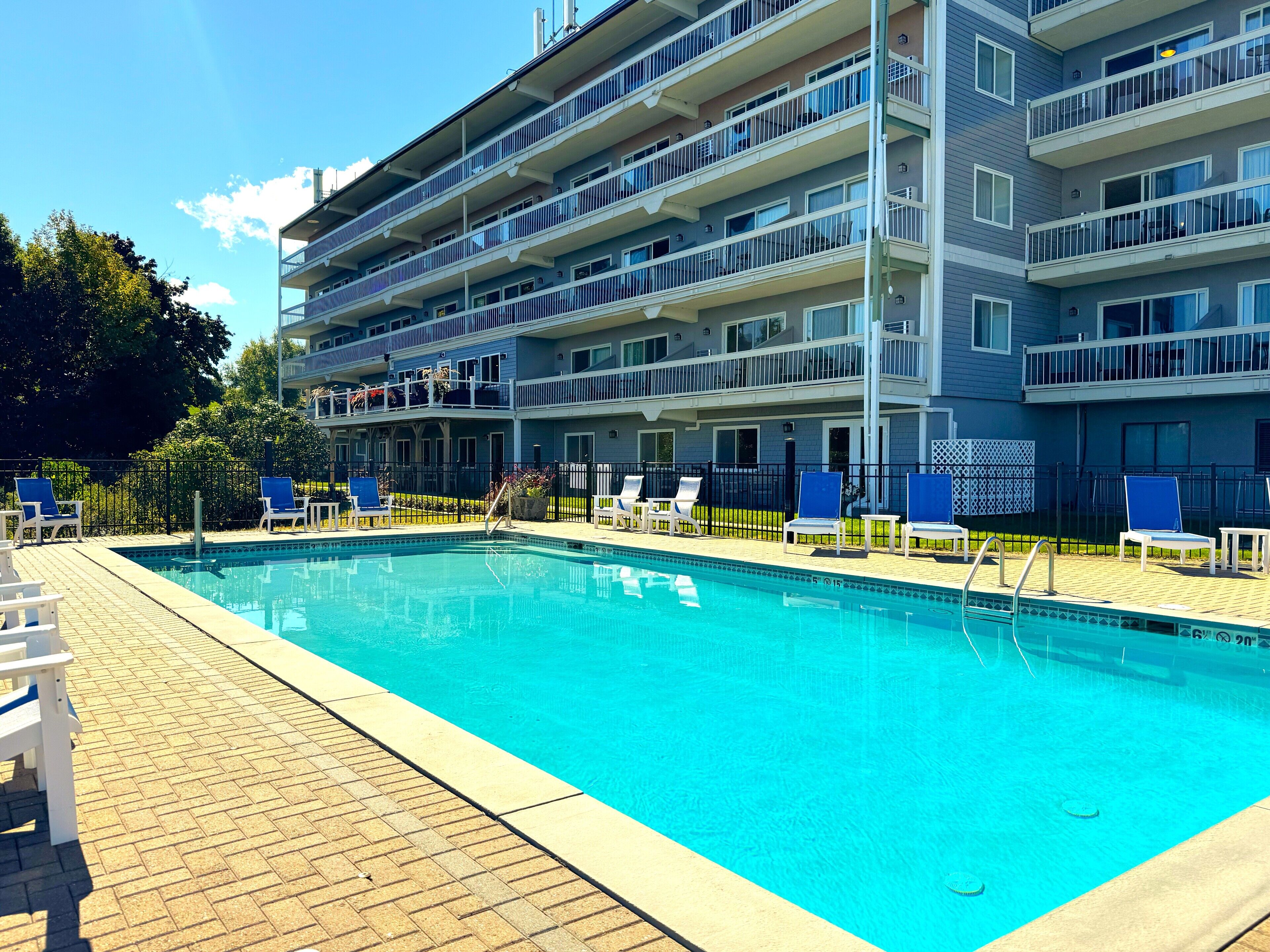 A multi-story hotel with a swimming pool, outdoor seating, and a fenced deck area.