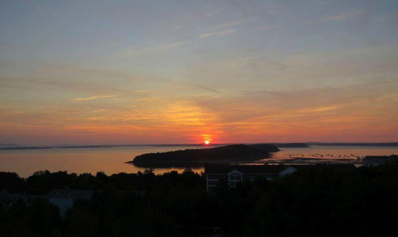 En solnedgång över en vattenyta med en liten ö och ett hus i förgrunden.